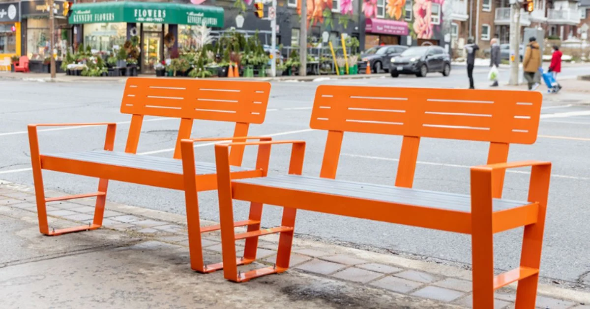 Bright orange metal benches placed along the sidewalk.
